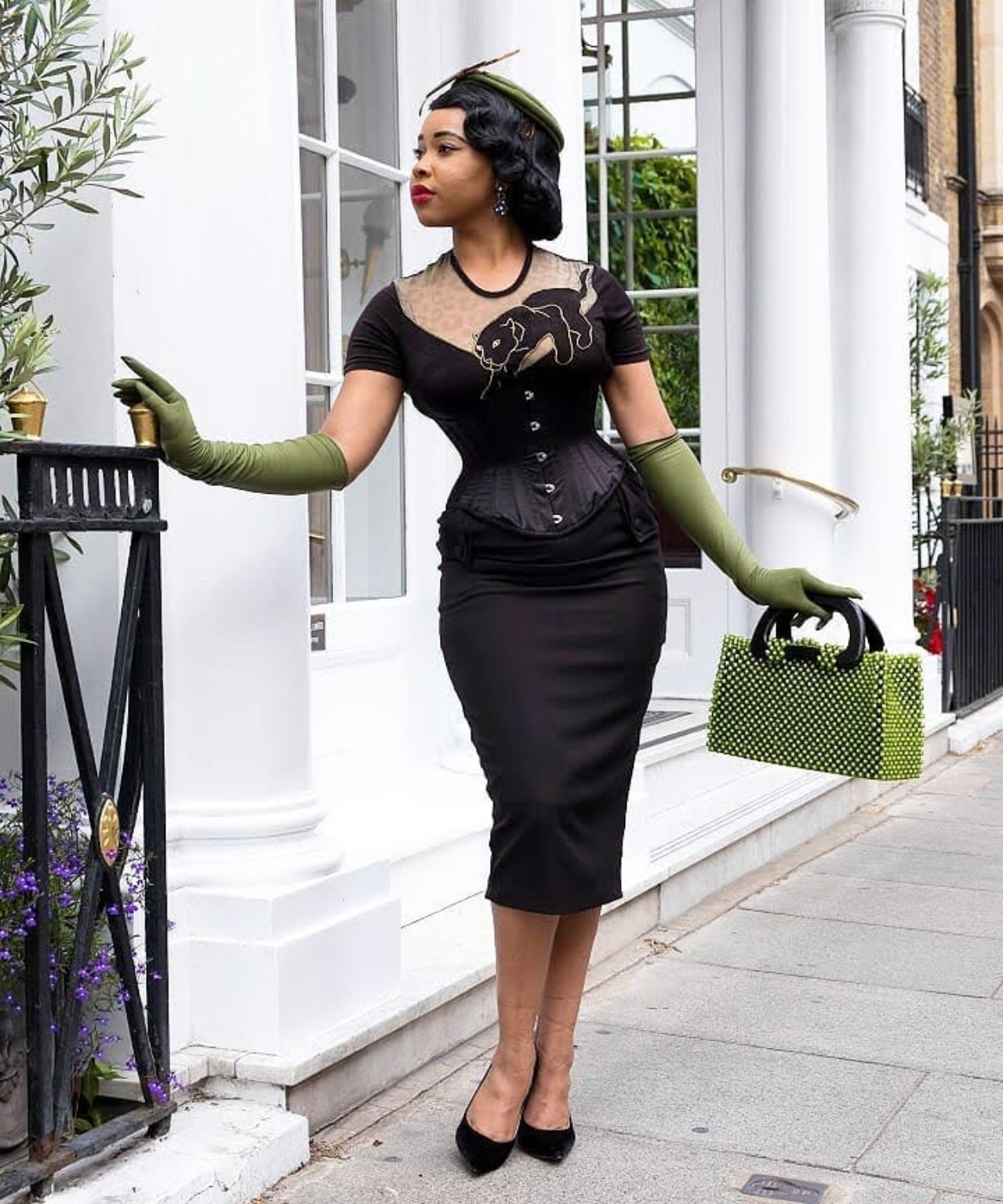 Lady E in a black dress with green hat, gloves and handbag