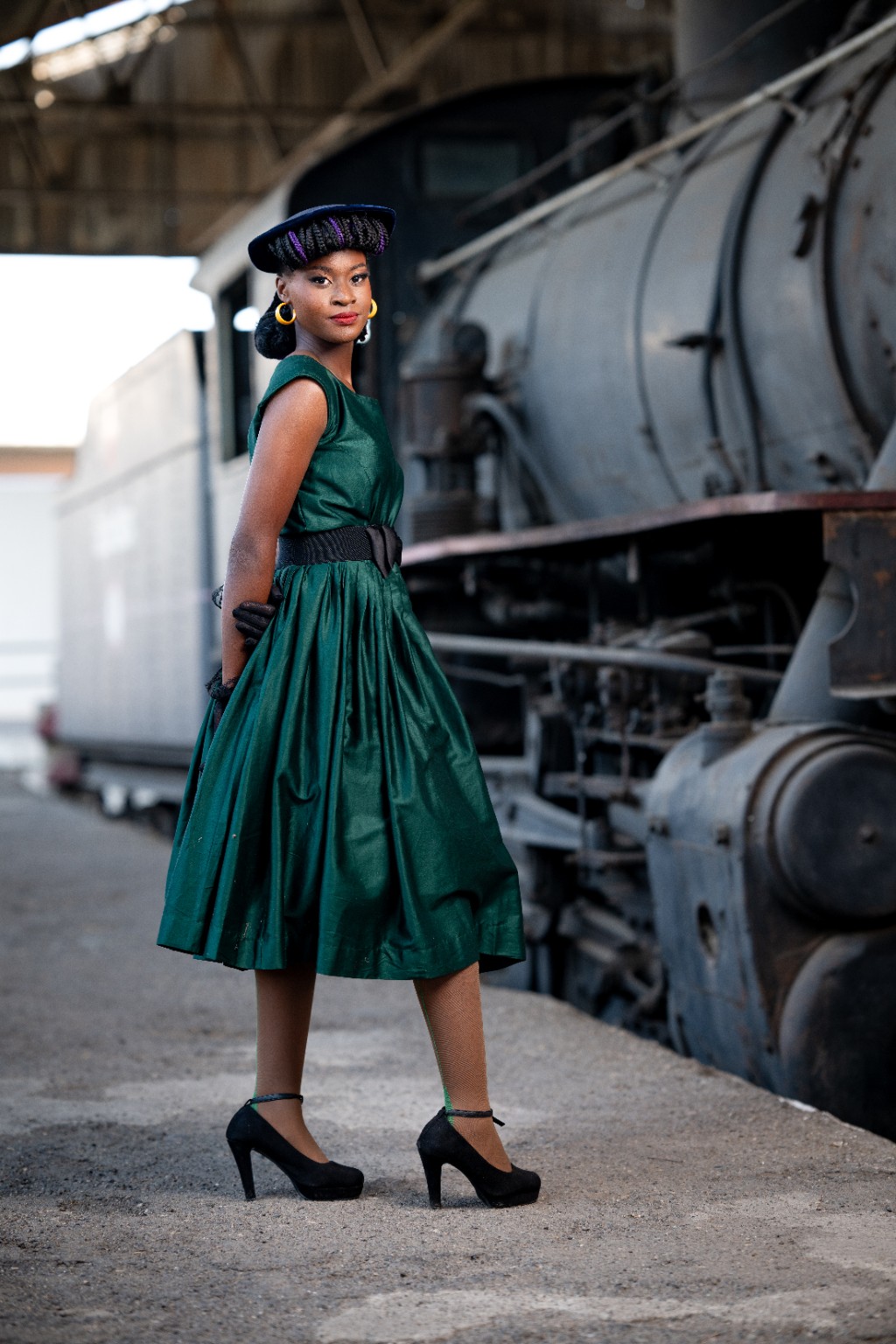 Finished vintage-inspired makeover with a green dress and hat beside a locomotive