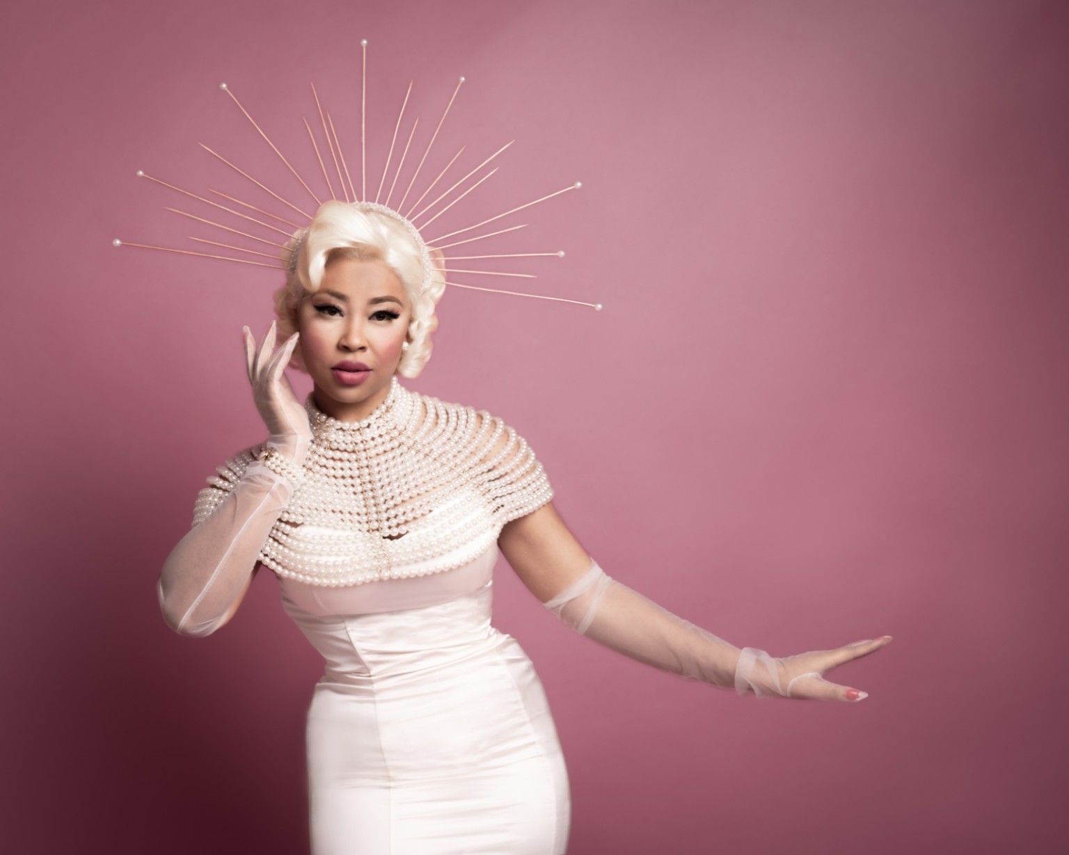 Lady E wearing pearls and a starburst crown against a pink background